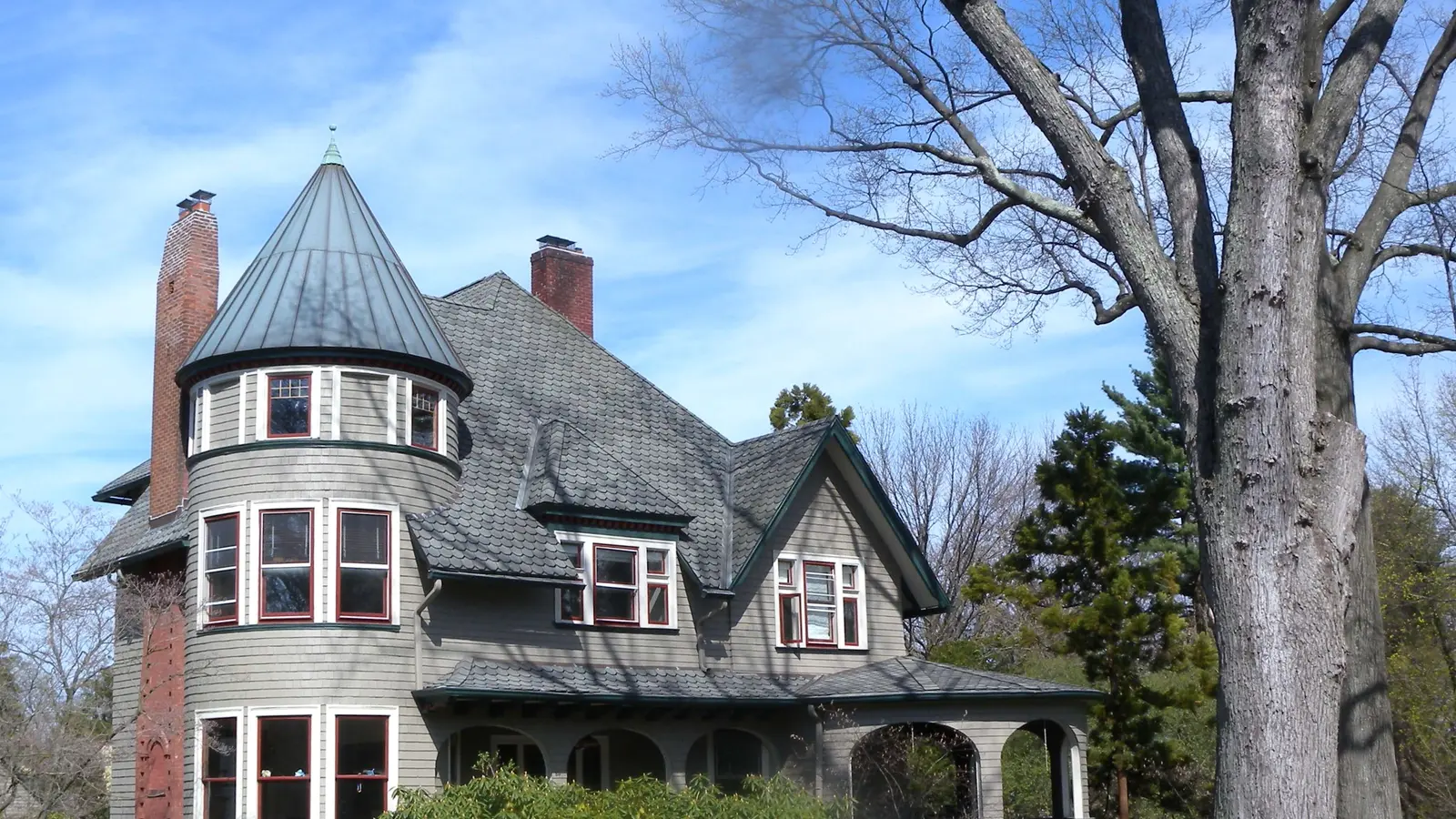 Large gray-shingled Victorian house with a round corner tower and a wraparound porch on Eagle Rock Way in Montclair, New Jersey, behind a bare tree