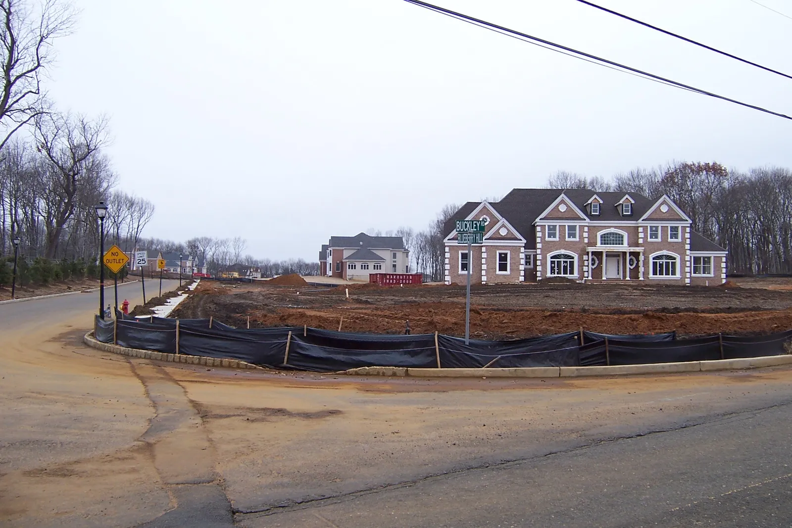 Large new two-story brick-front houses going up on cleared lots at a road corner in Marlboro Township, New Jersey, with silt fencing along the curb