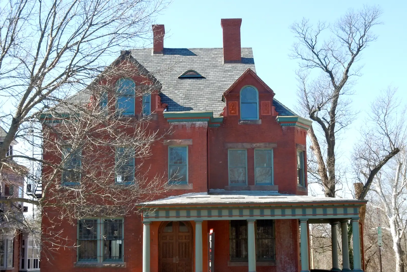 Three-story red brick house with a slate roof, tall chimneys and a green-trimmed front porch at 379 West State Street in Trenton, New Jersey