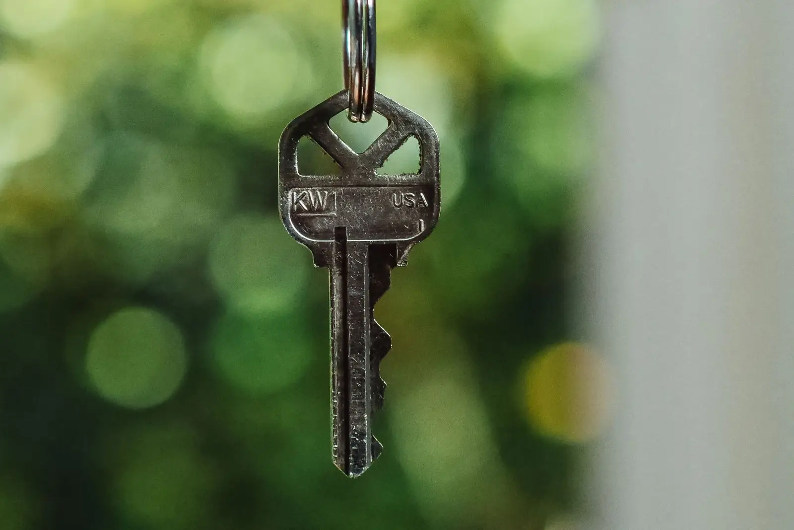 A single silver house key hanging from a key ring against a blurred green background