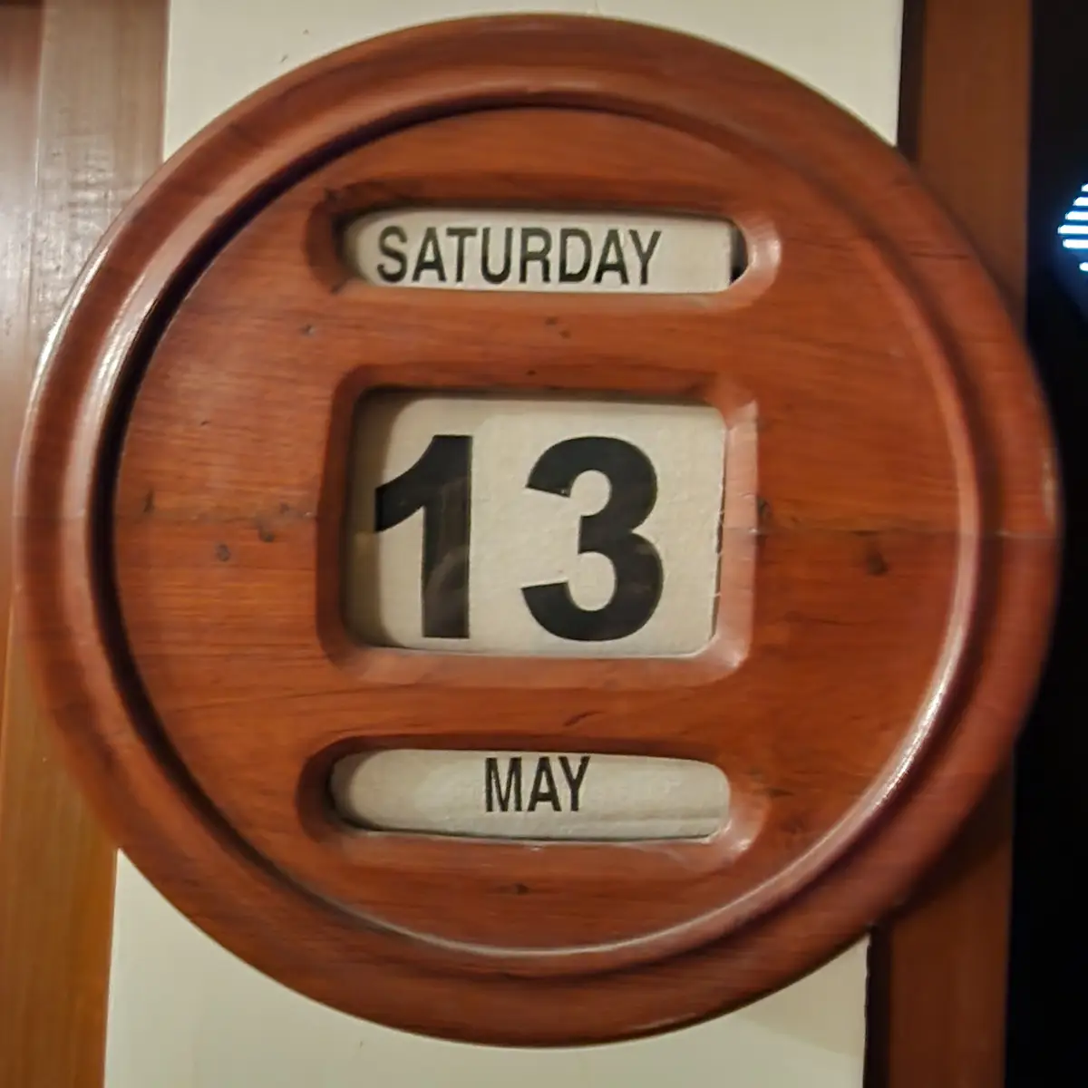 A round wooden wall calendar with flip cards showing Saturday, 13, May