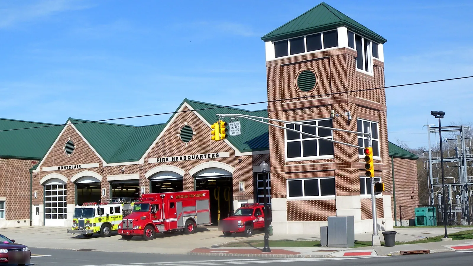 Montclair Fire Headquarters, a brick firehouse with a green roof and a square tower, with fire engines parked in front of its open bays