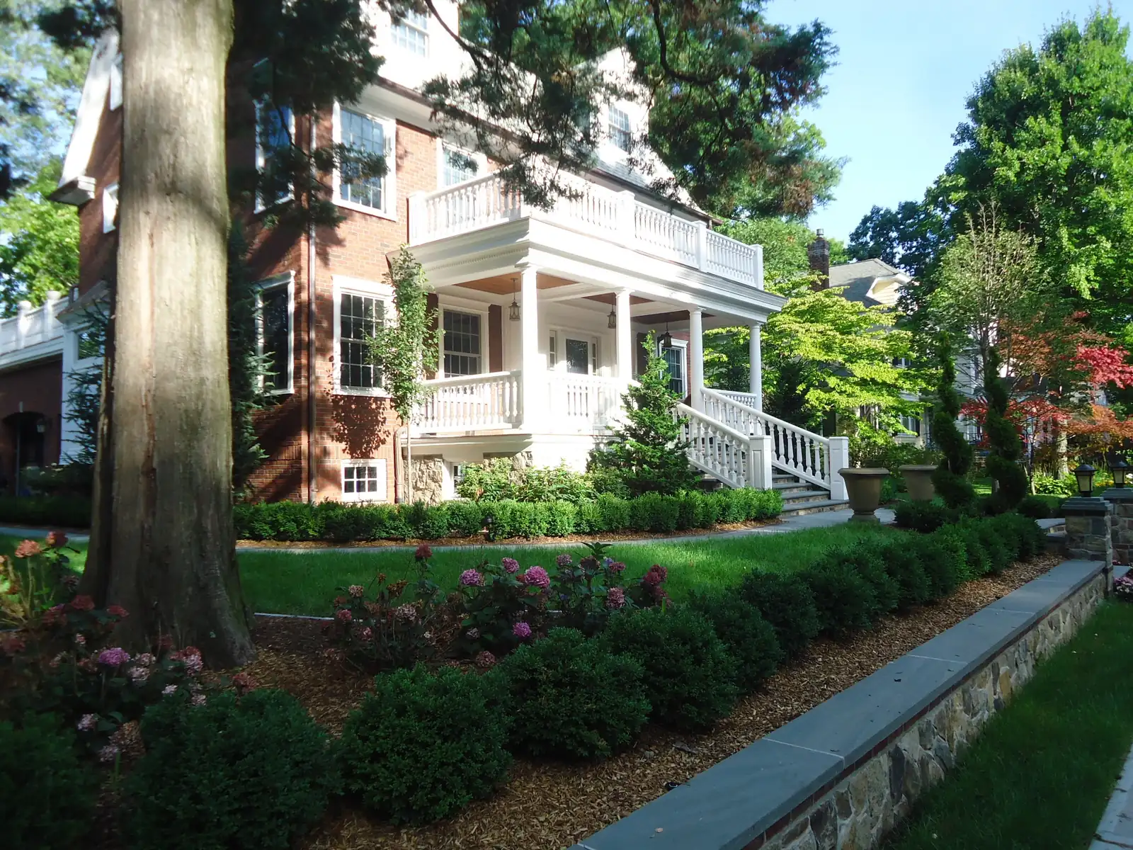Brick single-family house in Summit, New Jersey, with a white columned front porch, a balcony above and landscaped front garden beds