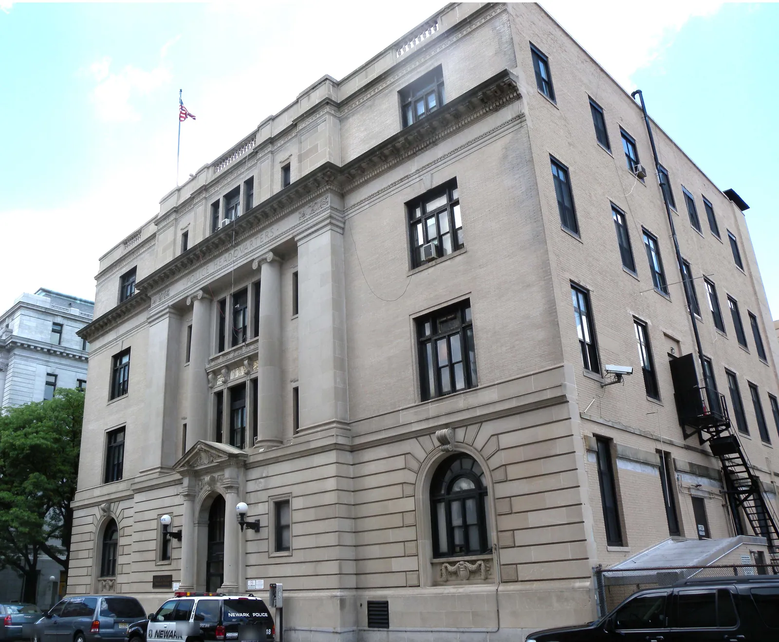 Newark Police headquarters, a four-story stone building with columns and 'Police Headquarters' carved above the entrance, a marked Newark police car parked outside