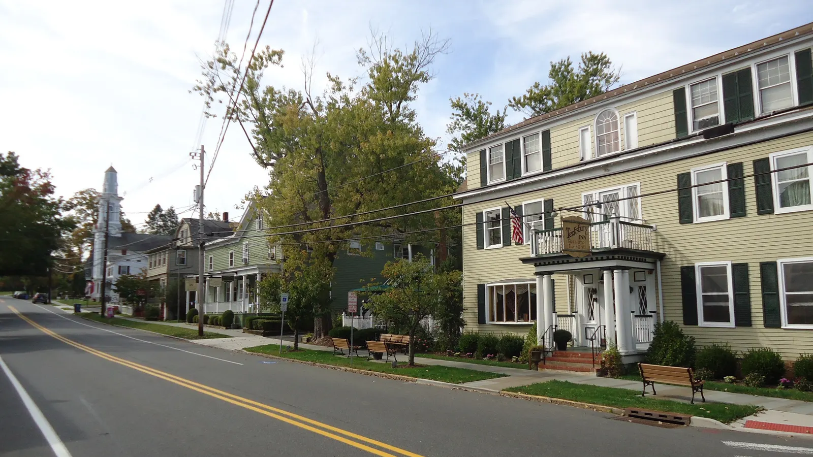 A street in Oldwick, New Jersey, with a three-story pale green building and older houses under autumn trees